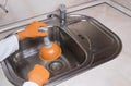 WomanÃ¢â¬â¢s hands with orange gloves cleaning sewer at kitchen faucet over sink. Close up of hand with plunger Royalty Free Stock Photo